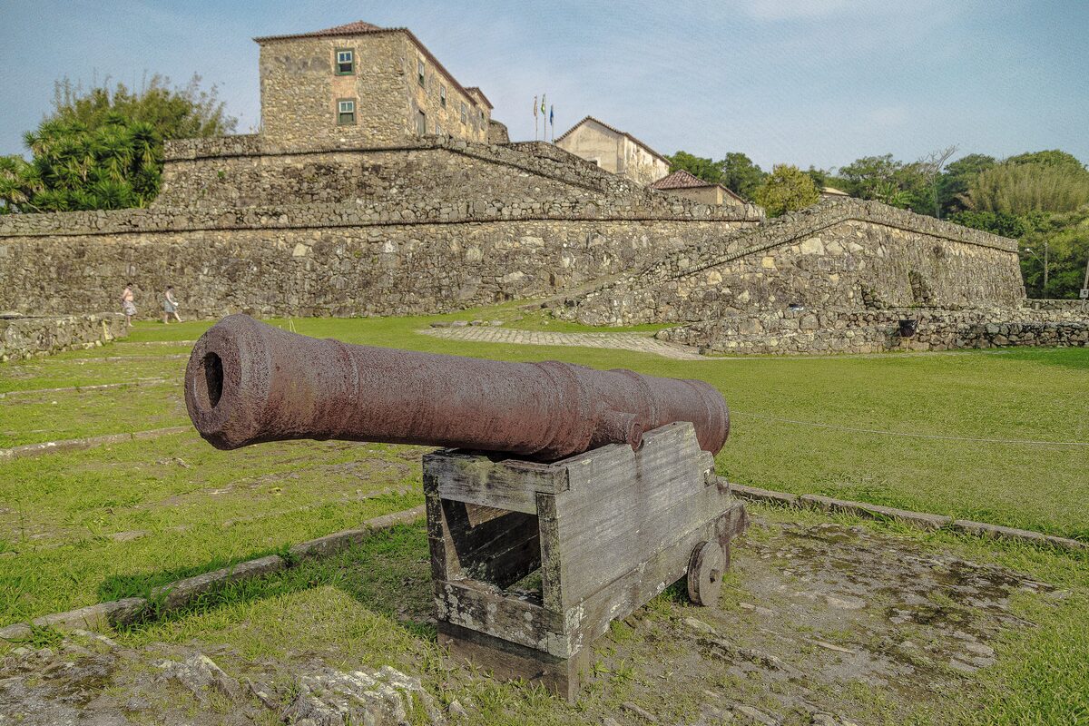 The stone walls and an old cannon of the São José da Ponta Grossa fortress on grass below the fortress buildings