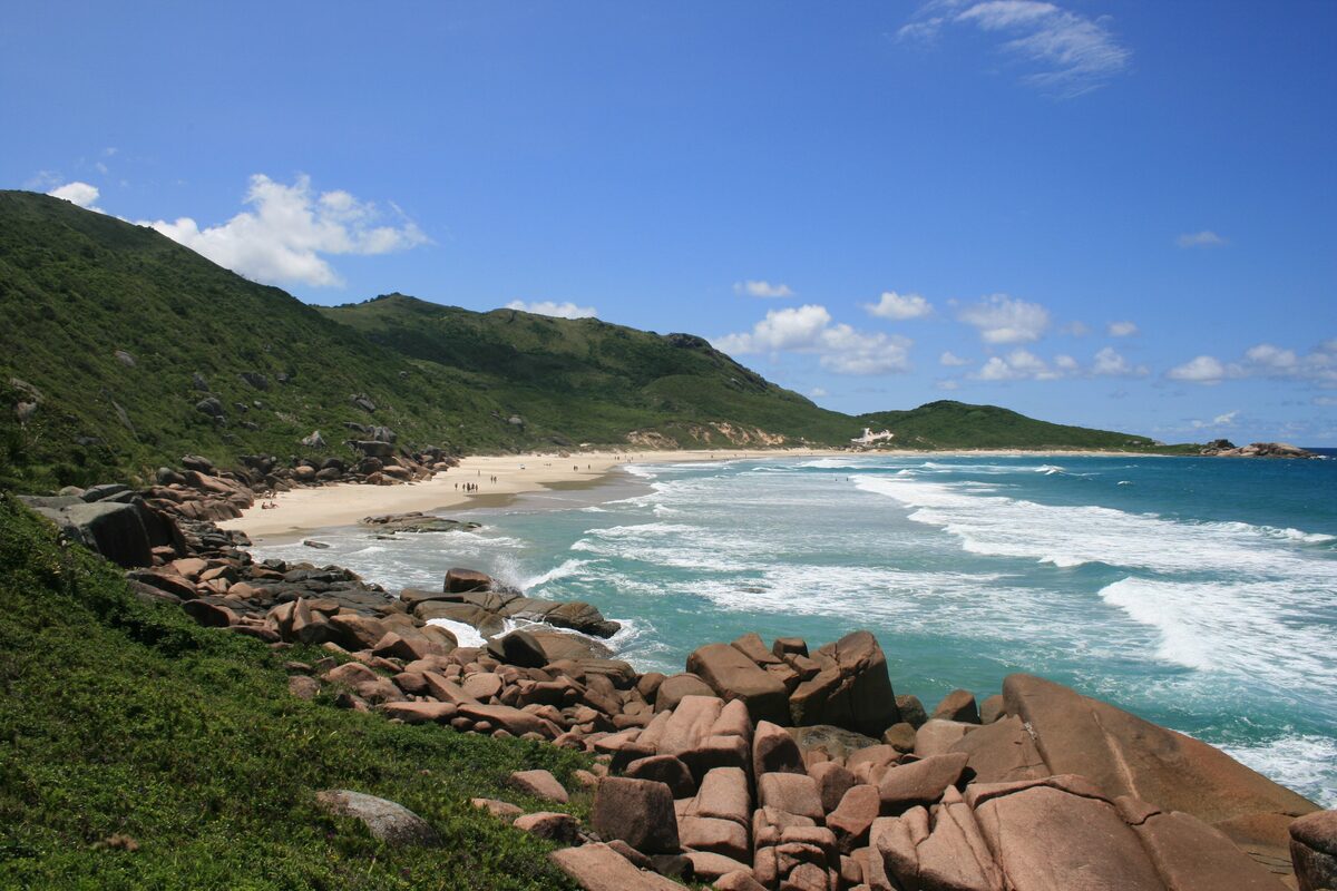 Granite boulders and a sandy cove at Praia da Galheta, with waves breaking on the rocks in bright sun