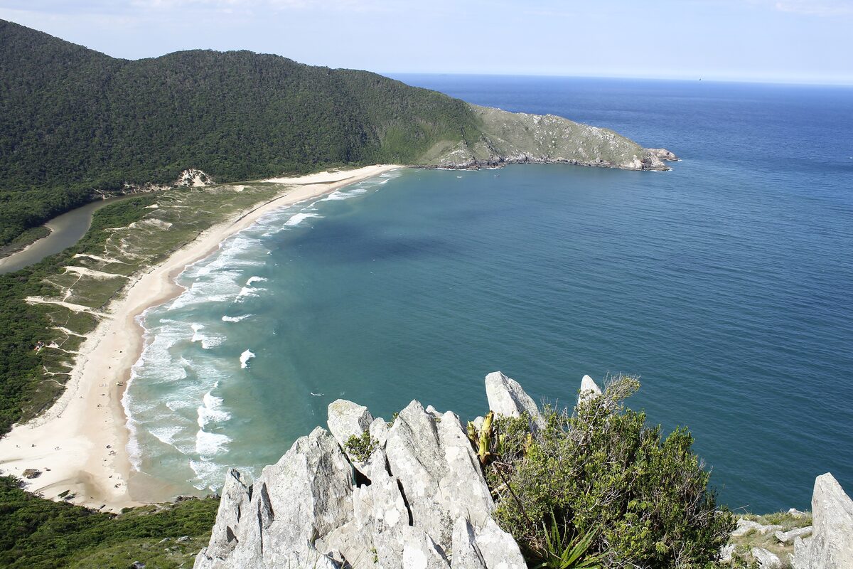 Lagoinha do Leste from the cliff above: a curved white beach between green hills and grey rock, with surf in the bay