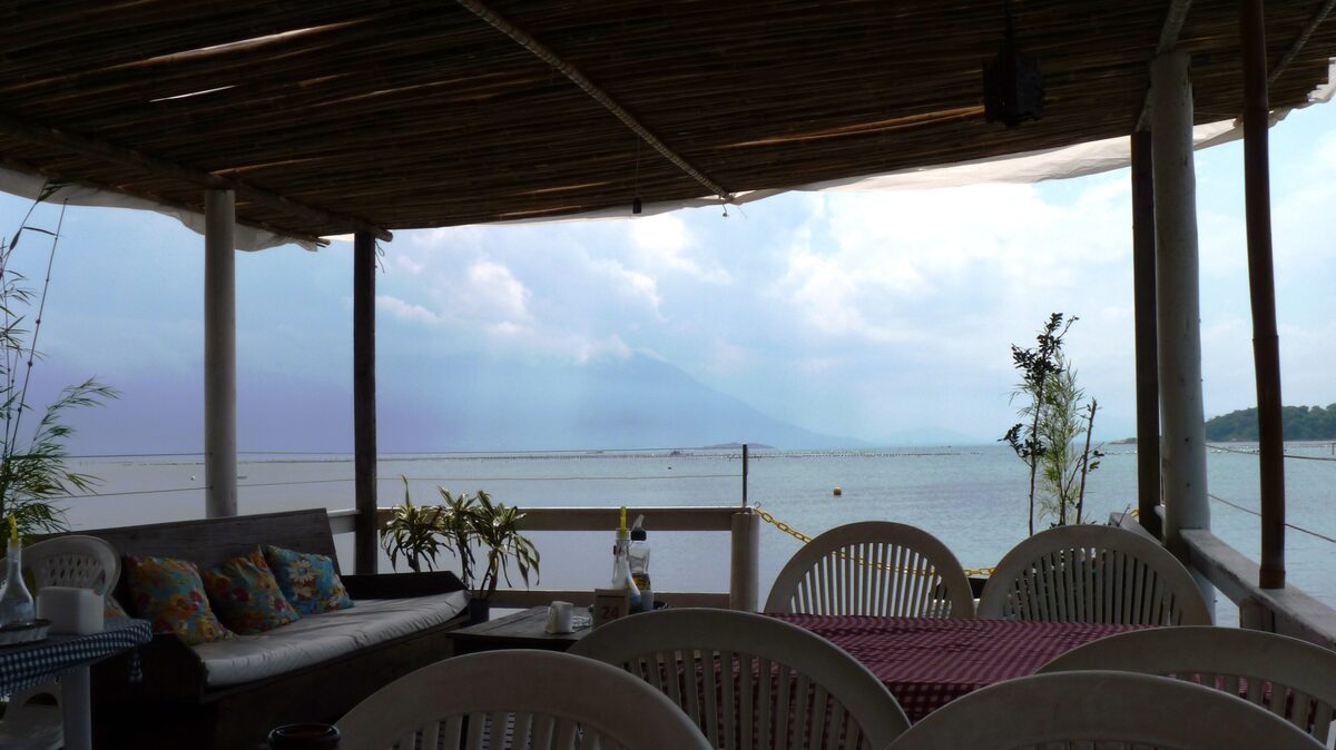 The covered terrace of a waterfront restaurant in Ribeirão da Ilha, with tables facing the bay and hazy mountains across the water