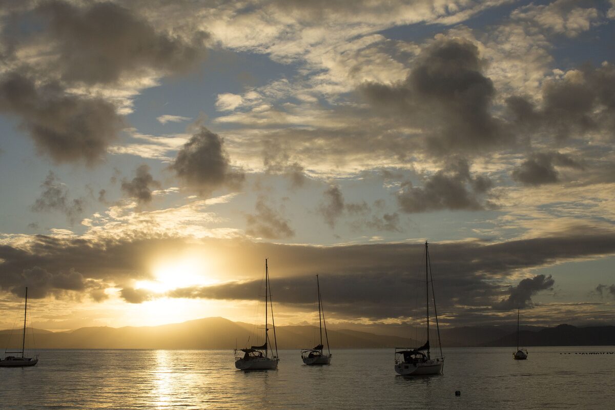 Sailboats at anchor silhouetted against a low sun and clouds over the bay at sunset