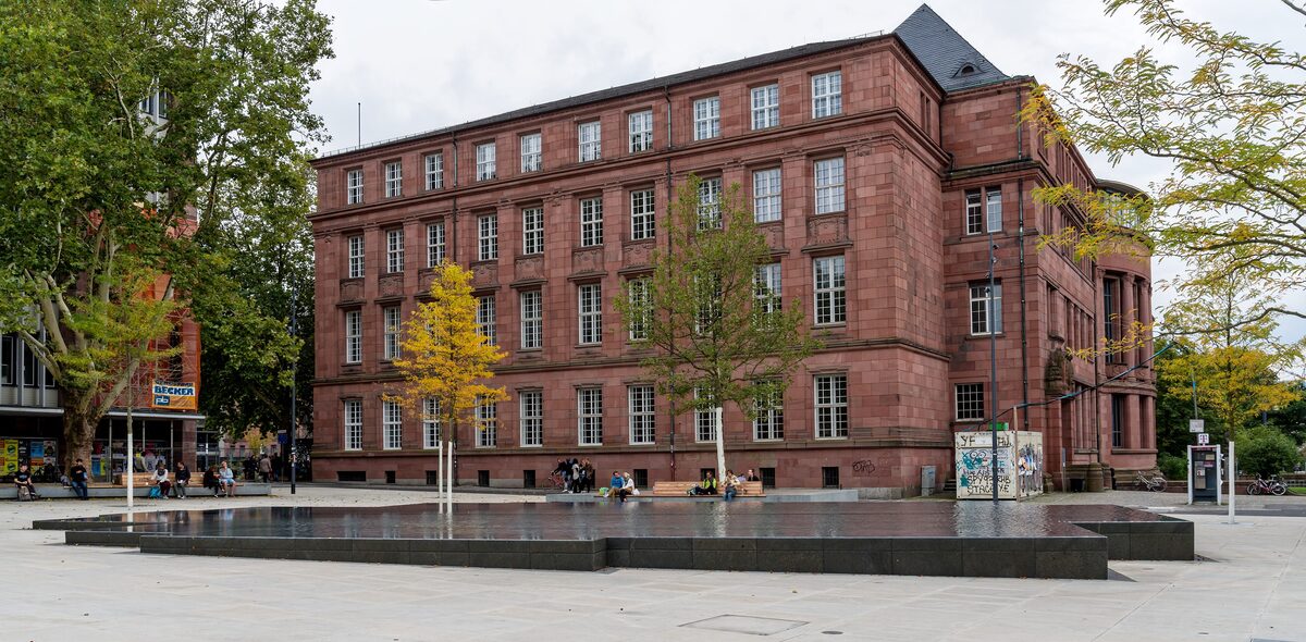 The red sandstone university building on the Platz der Alten Synagoge, with the memorial fountain basin in front