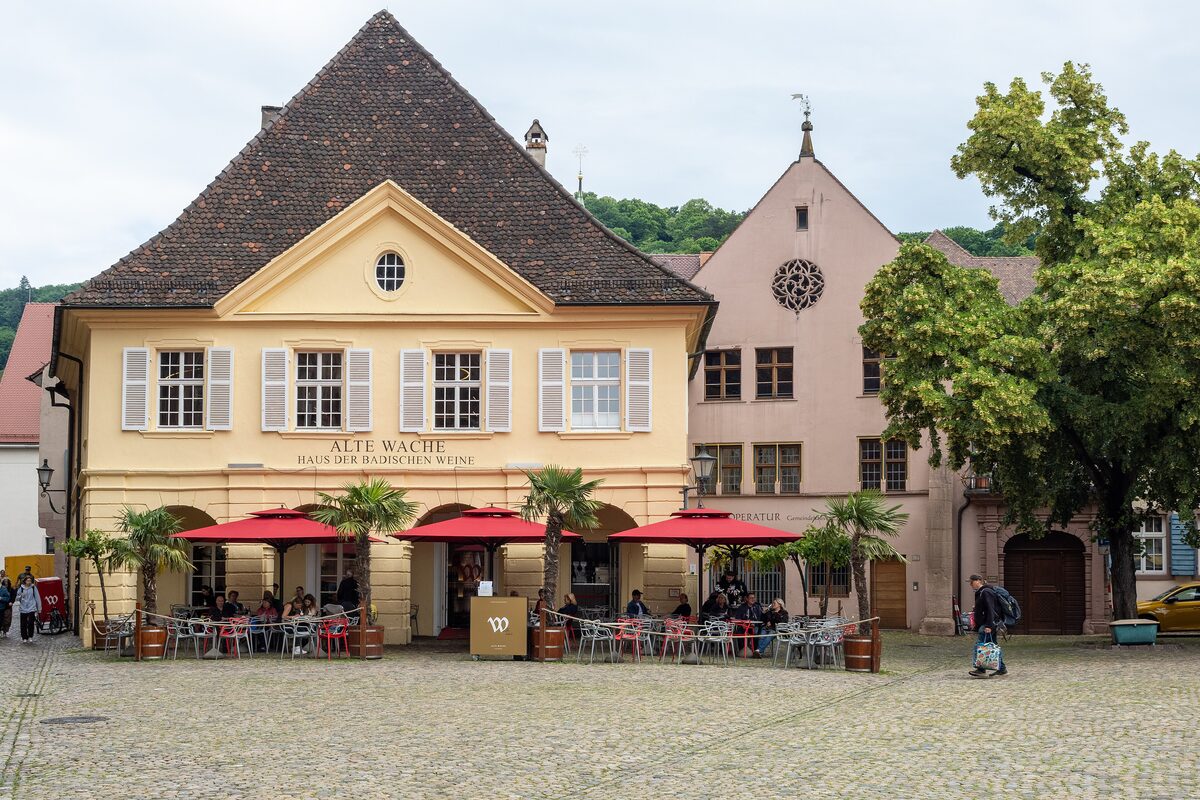 The yellow Alte Wache on Münsterplatz with red parasols and palm trees on its terrace