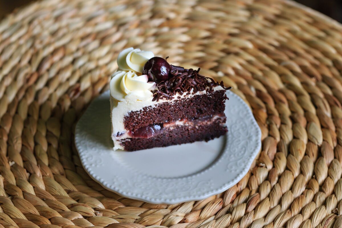 A slice of Black Forest cake with whipped cream and a cherry on a white plate