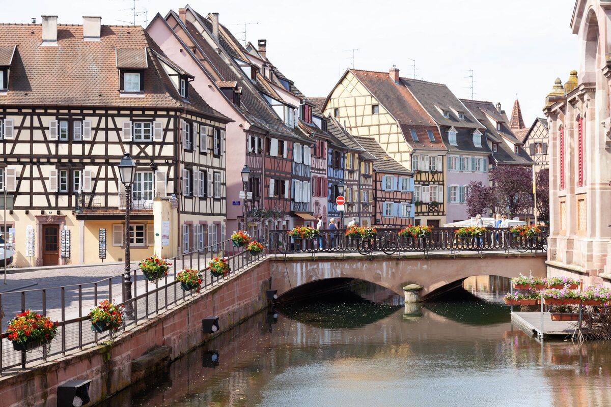 Half-timbered houses and a stone bridge over a canal in Colmar, with flower boxes on the railings