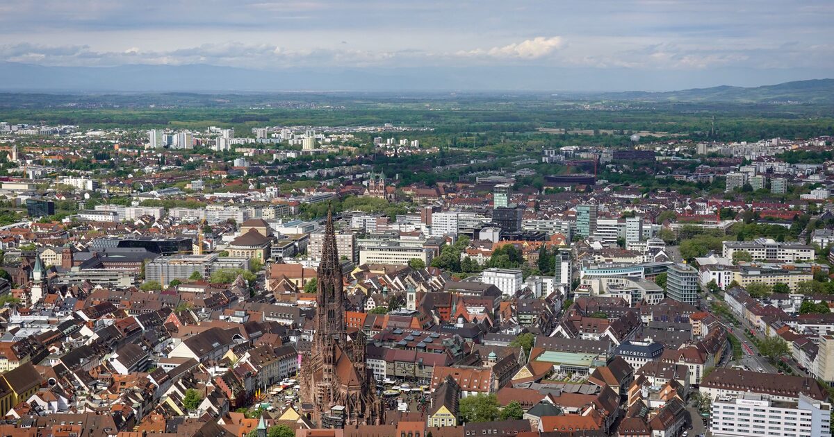 Aerial view of Freiburg's rooftops with the Minster spire rising from the old town and the Rhine plain fading into haze behind