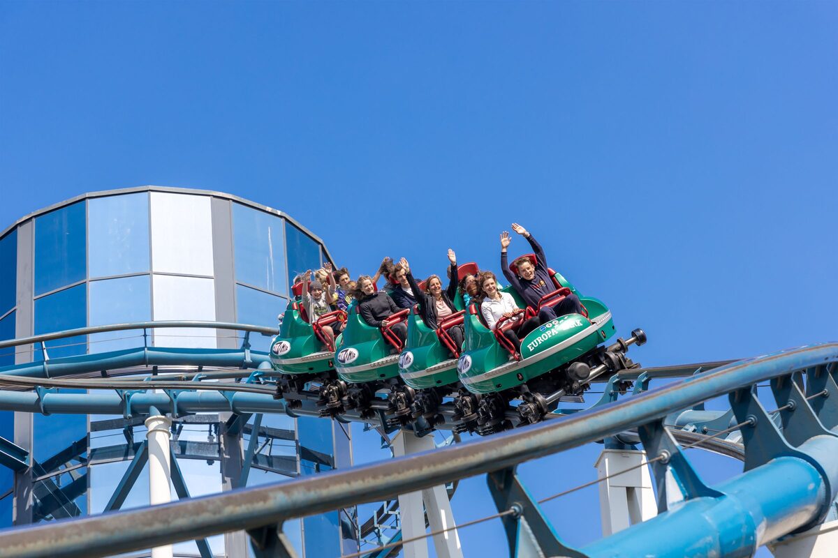 Riders with raised arms on a green roller coaster at Europa-Park under a blue sky