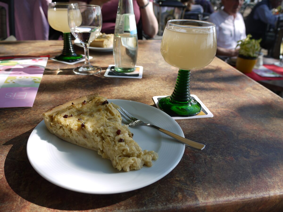 A slice of Zwiebelkuchen on a plate and two glasses of Federweißer on a sunlit table