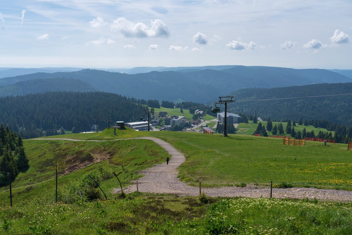A gravel path across the Seebuck summit meadow, with a ski lift and Feldberg village below and forested ridges beyond