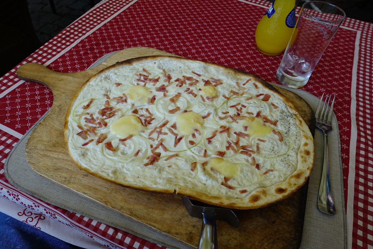 A Flammkuchen topped with onions, bacon and dots of Munster cheese on a wooden board