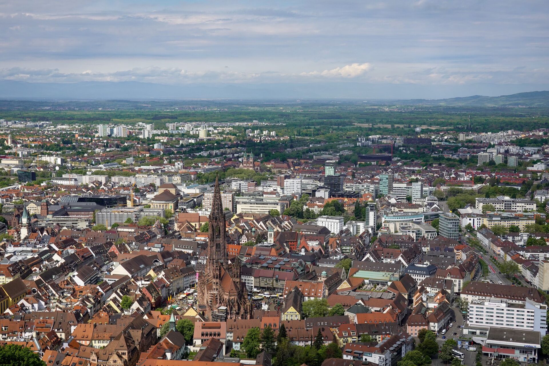 Aerial view of Freiburg's rooftops with the Minster spire rising from the old town and the Rhine plain fading into haze behind