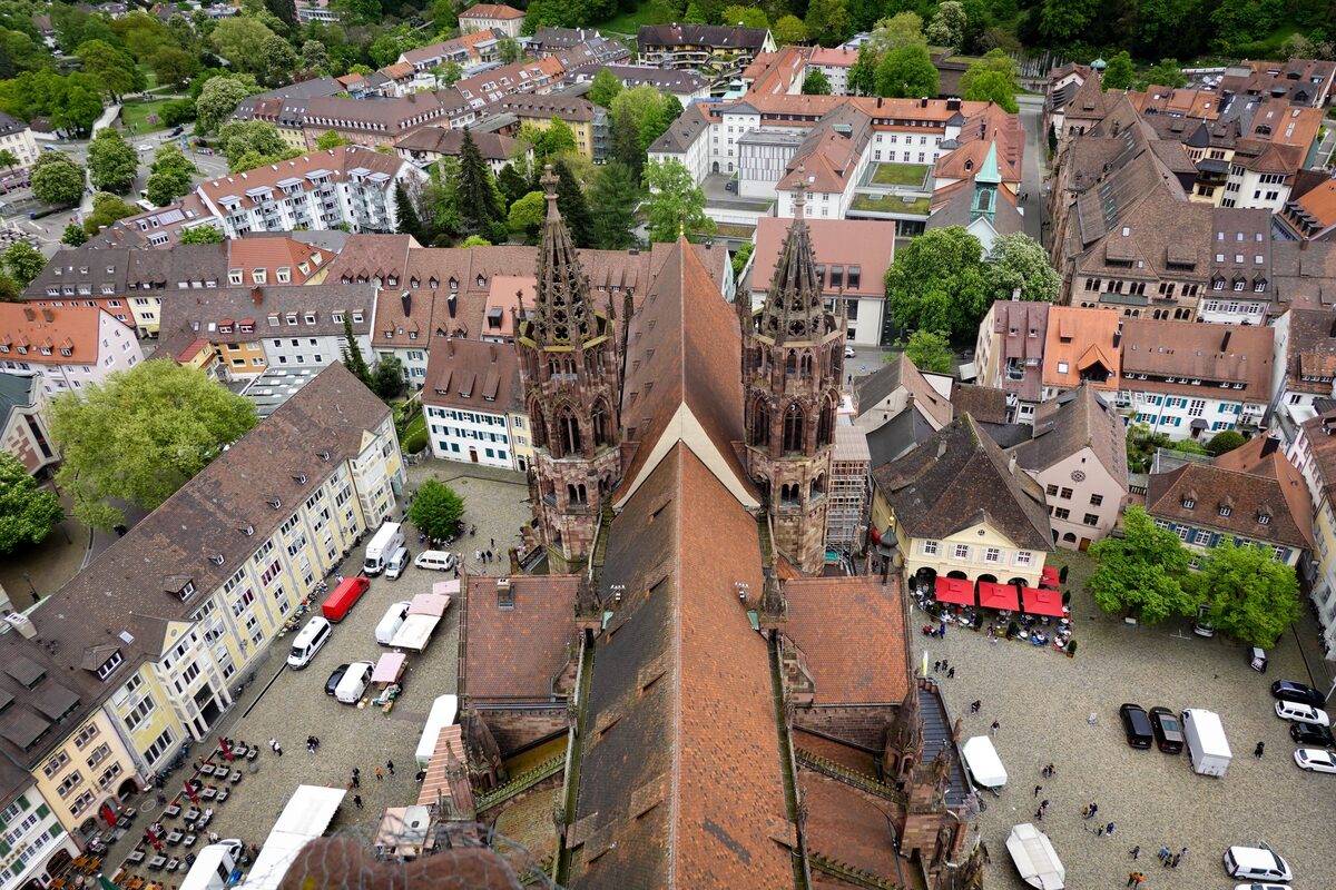 Aerial view of Münsterplatz in Freiburg with market stalls and red umbrellas beside the Minster's roof and towers