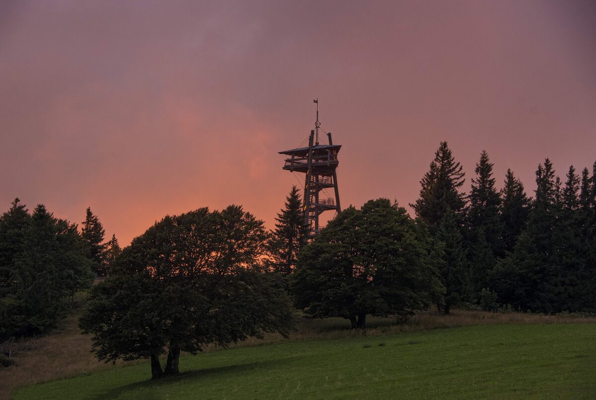 The lookout tower on the Schauinsland summit against a red evening sky, with trees in the foreground