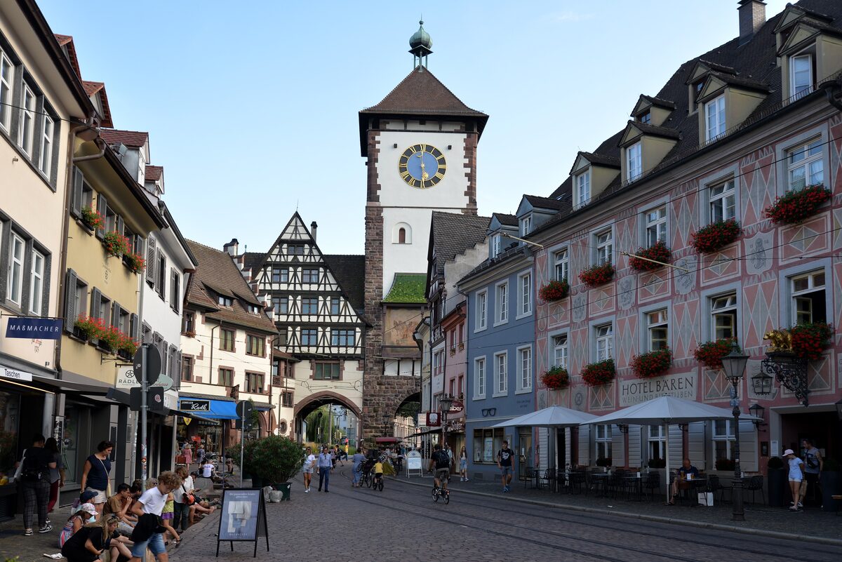 The Schwabentor clock tower at the end of a pedestrian street lined with painted houses and flower boxes