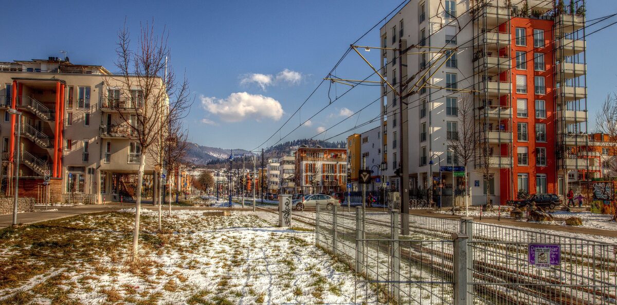 Modern apartment blocks and tram tracks in the Vauban district, with the Black Forest hills behind