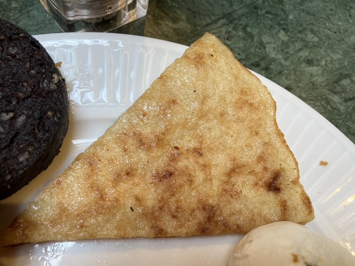 A golden triangle of boxty, the Irish potato pancake, on a white plate next to black pudding