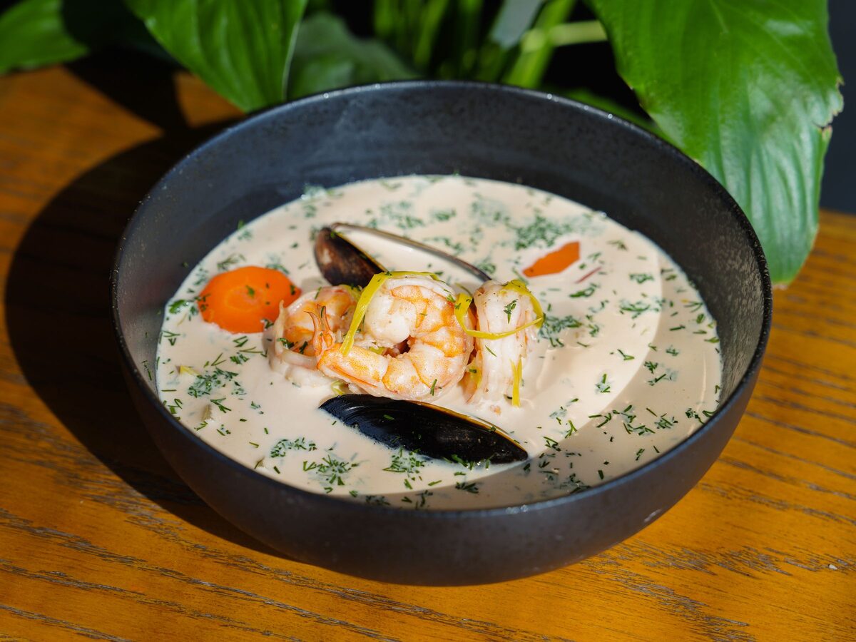 A bowl of creamy seafood chowder with prawns, mussels and carrot, sprinkled with dill