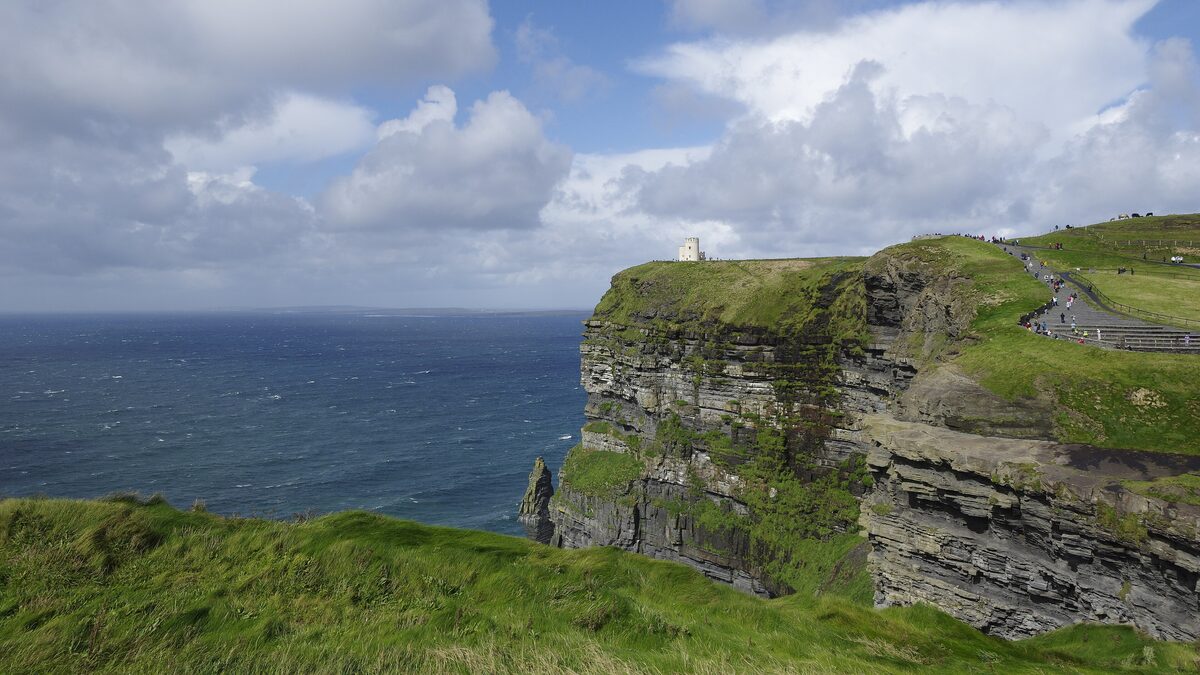 The layered dark cliffs of Moher dropping straight into the Atlantic, with green grass on top and O'Brien's Tower on the headland