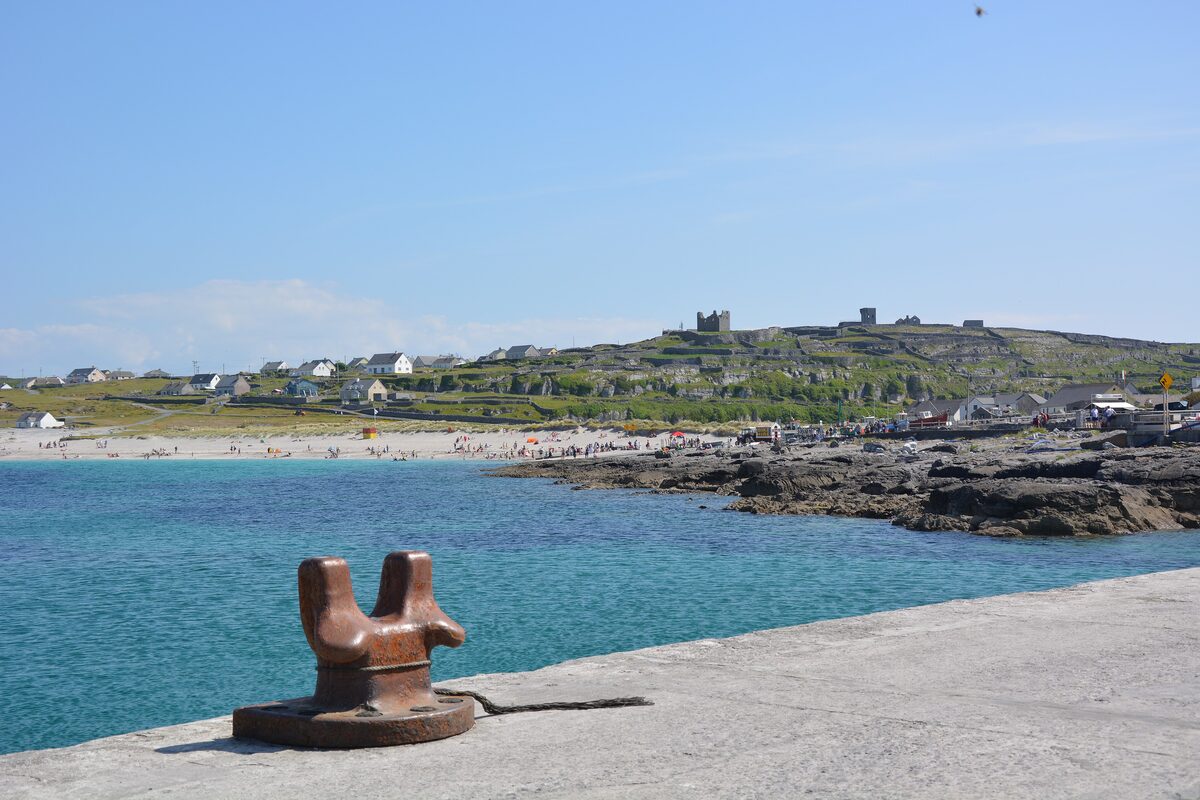 The turquoise water and white beach of Inis Oírr seen from the pier, with the village and the ruined castle on the hill behind