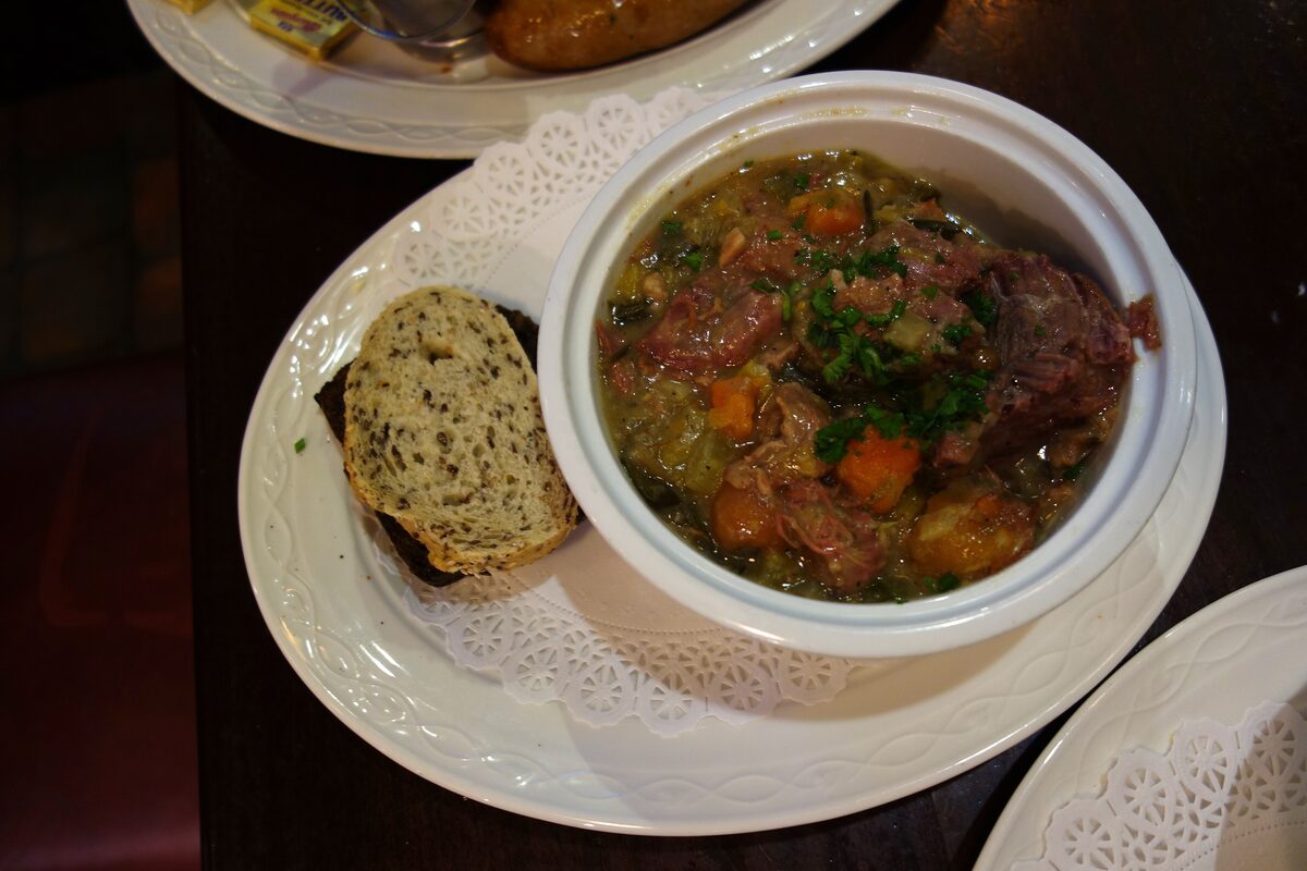 A bowl of Irish stew with lamb and vegetables, with a slice of brown bread on the side