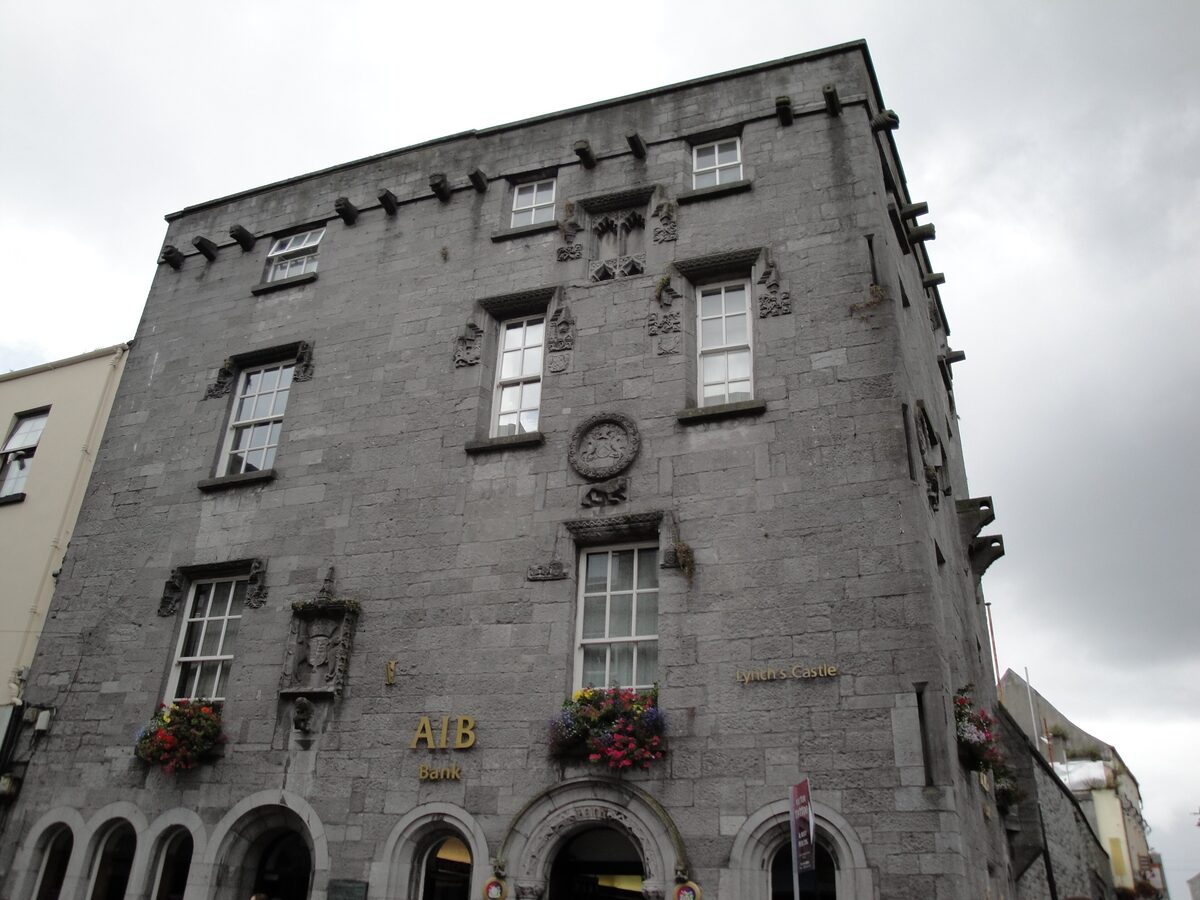 Lynch's Castle on Shop Street, a gray stone tower house with carved coats of arms and window frames, now a bank with flower boxes on the ground floor