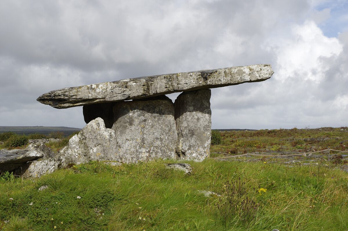 Poulnabrone Dolmen, a huge flat capstone on upright stone slabs, standing on the limestone and grass of the Burren under a cloudy sky