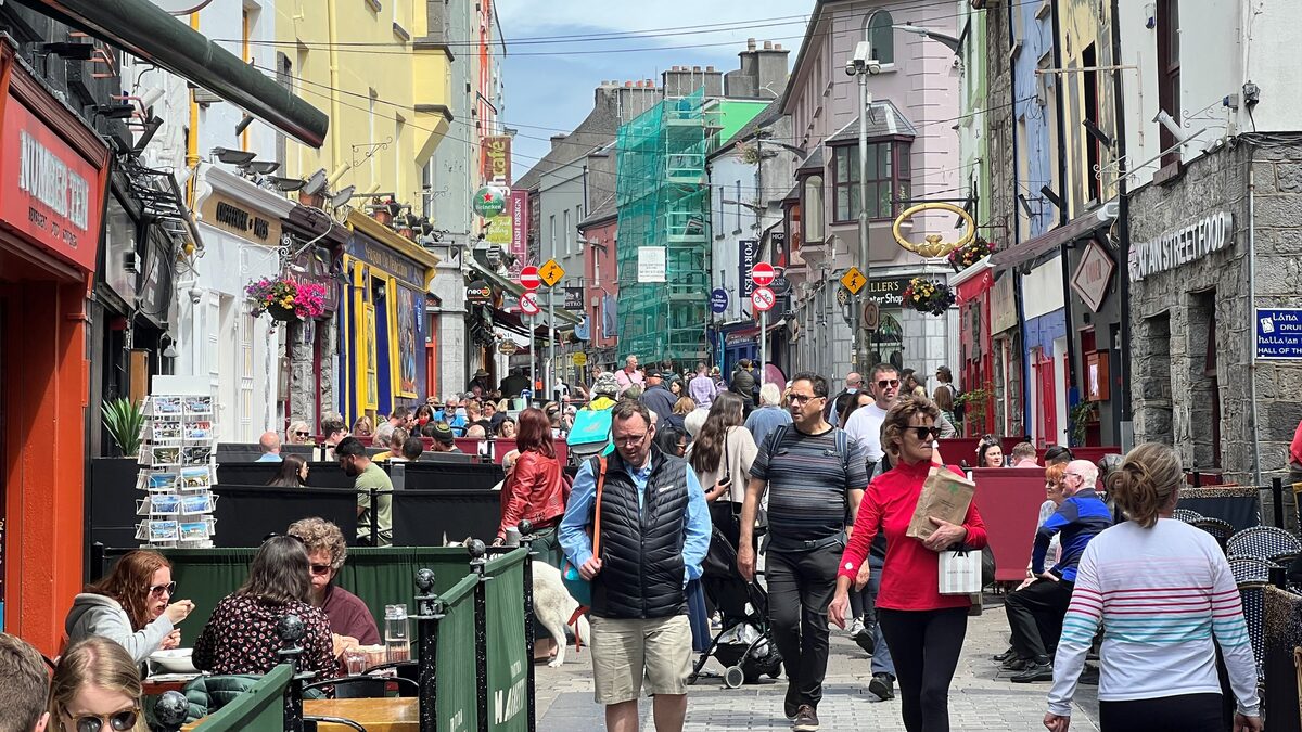 Quay Street in Galway on a busy day, with colorful shopfronts and pub signs and crowds walking between café tables