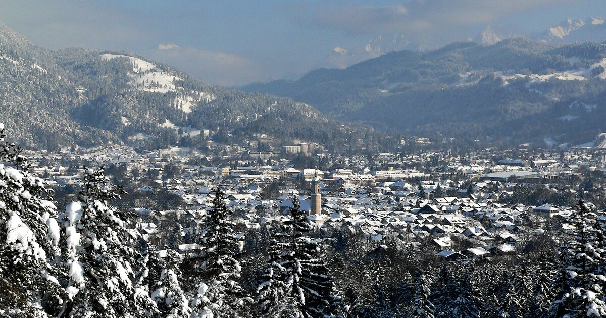 Snowy rooftops of Garmisch-Partenkirchen seen through snowy firs, with the Wetterstein ridge hazy behind