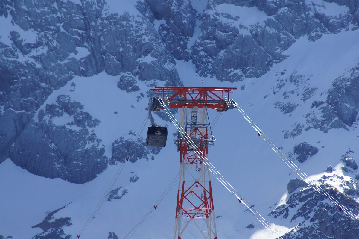 An Eibsee cable car cabin beside a red steel pylon, high on the snowy rock face below the Zugspitze