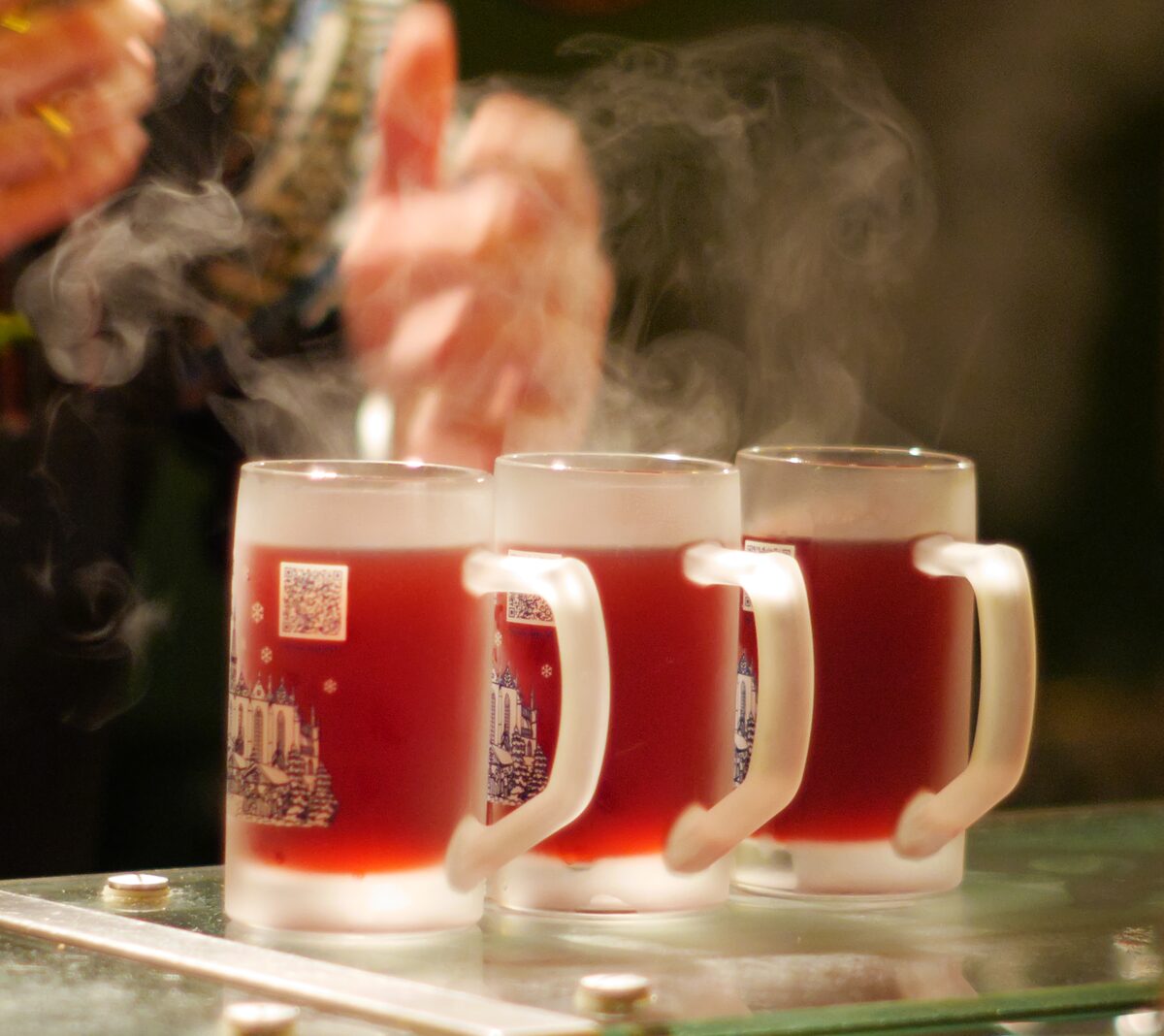Three frosted mugs of steaming mulled wine on a counter at a winter market