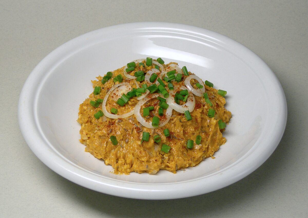 A plate of Obatzda, the orange cheese spread, with onion rings and chopped herbs on top