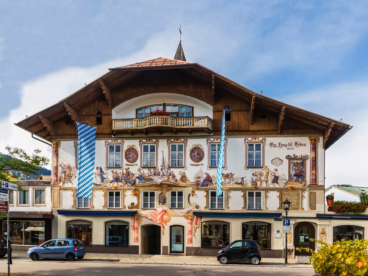 A large painted house on the main street of Oberammergau, its facade covered in frescoes, with Bavarian flags