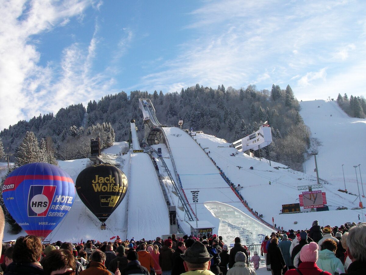A crowd packed into the Olympic ski stadium on New Year's Day, with the snow-covered ski jumps behind and two hot-air balloons