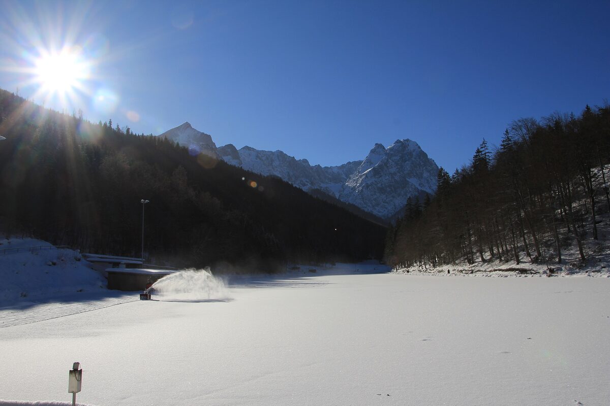 The Riessersee lake frozen in winter, with snowy mountains and dark forest around the shore in bright sun
