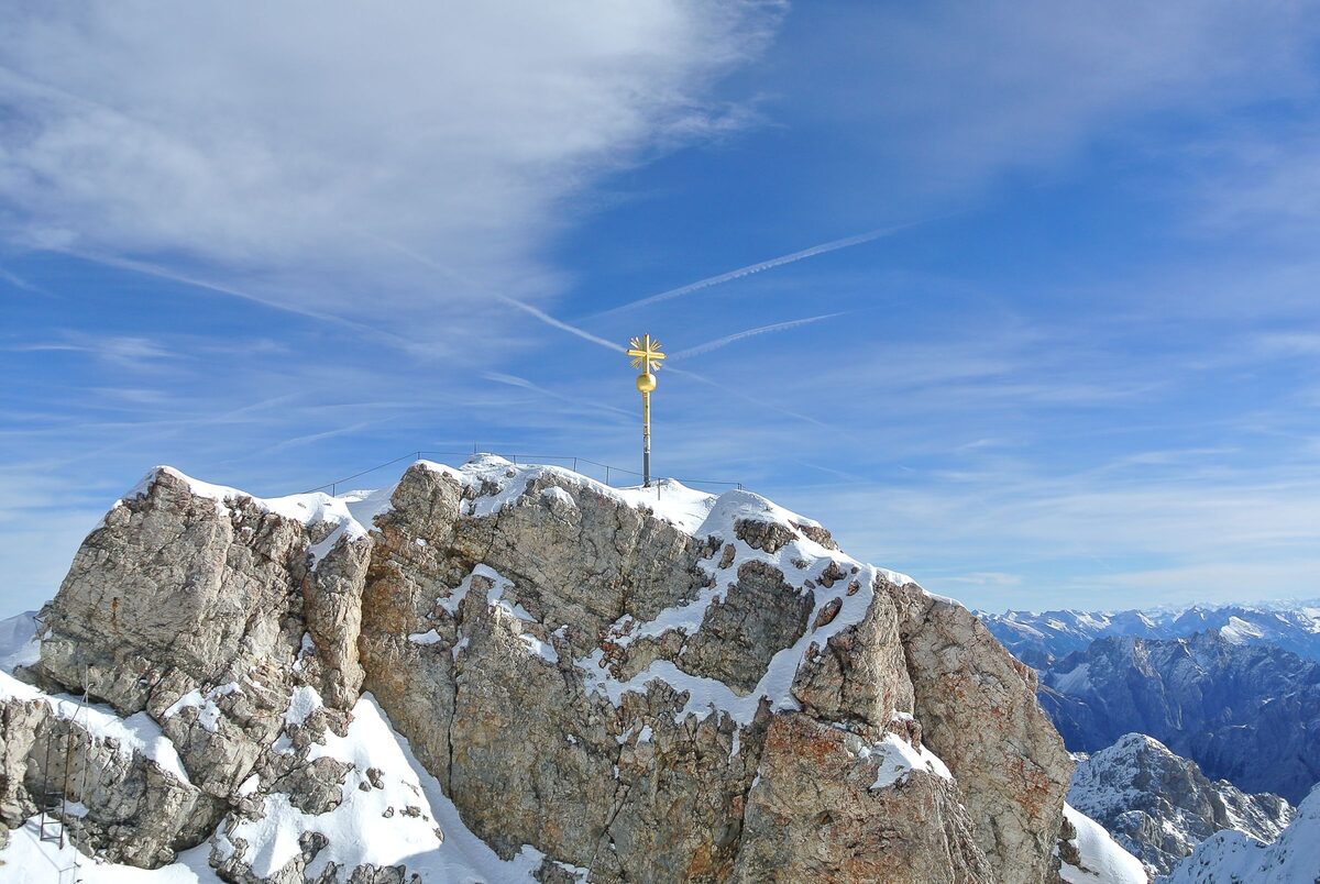 The golden summit cross on the snowy rock of the Zugspitze, Germany's highest mountain, under a blue winter sky