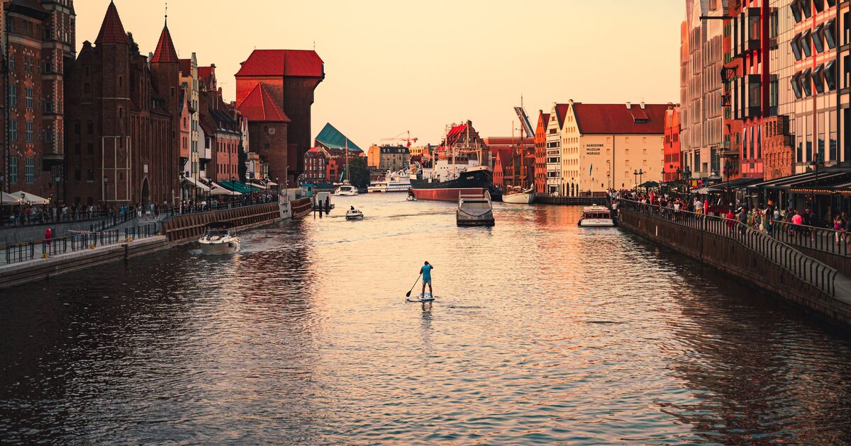 Sunset over the Motława river in Gdańsk, with the brick Crane and the gabled houses of the Long Riverfront and a paddleboarder on the water