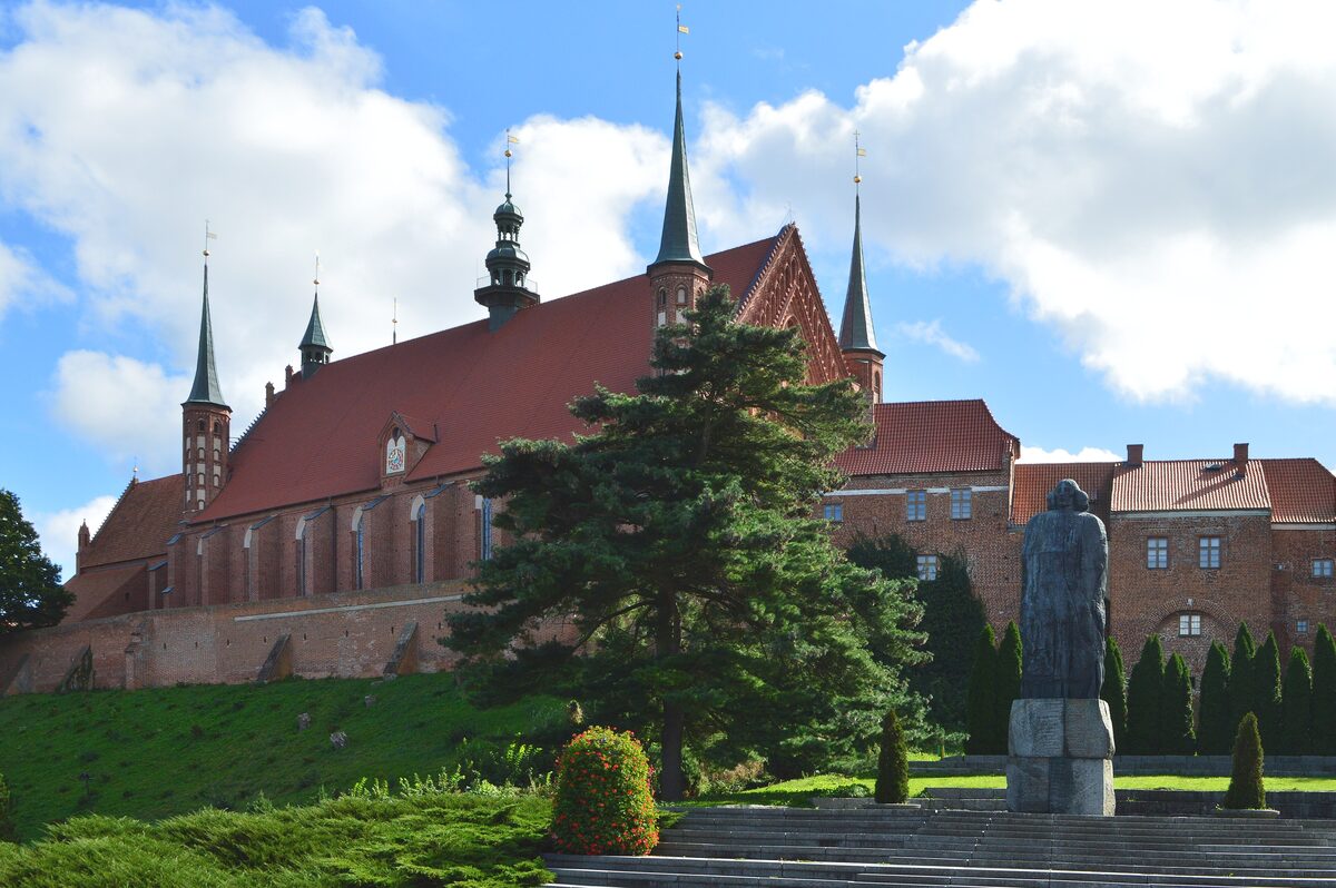 Frombork Cathedral, a red brick Gothic church with spired corner towers, above a lawn with the Copernicus statue