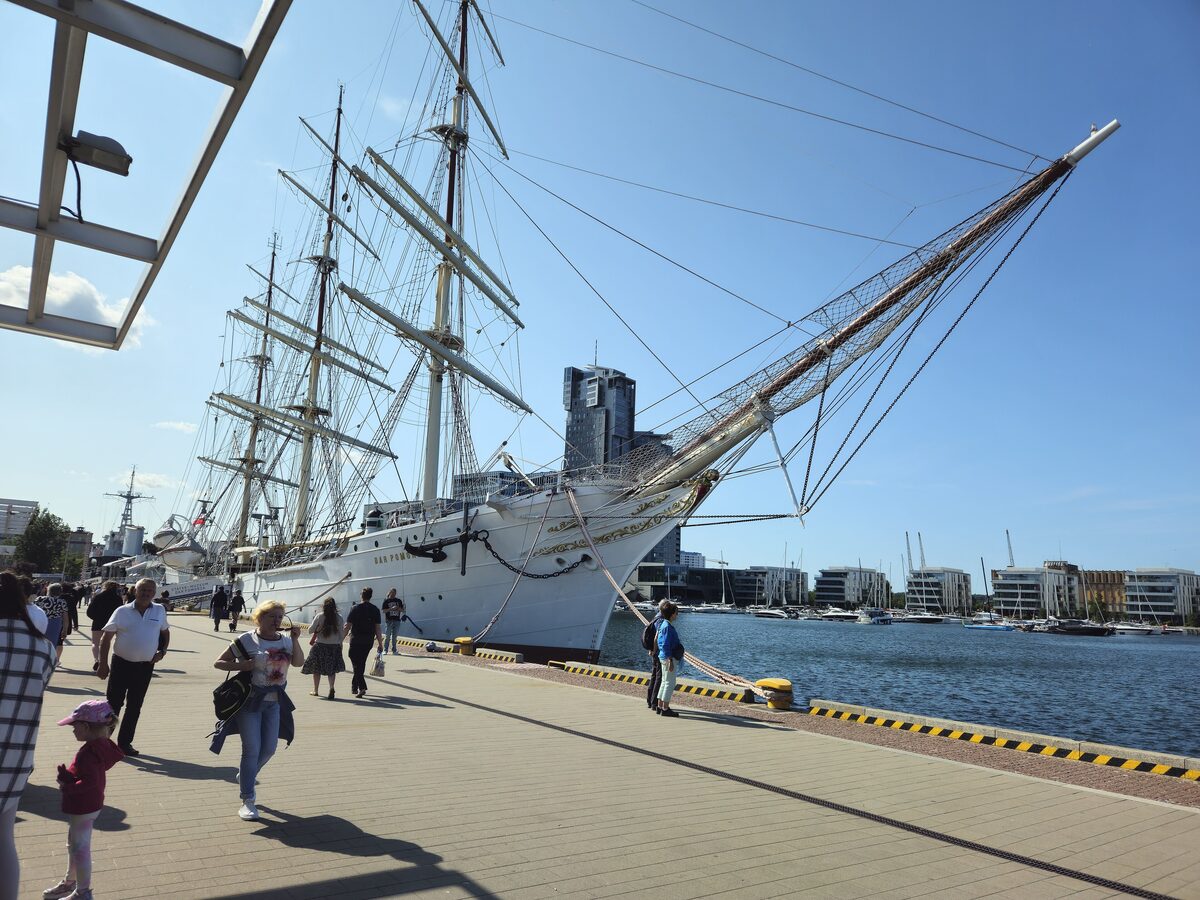 The white tall ship Dar Pomorza moored on the pier in Gdynia, with people walking along the quay