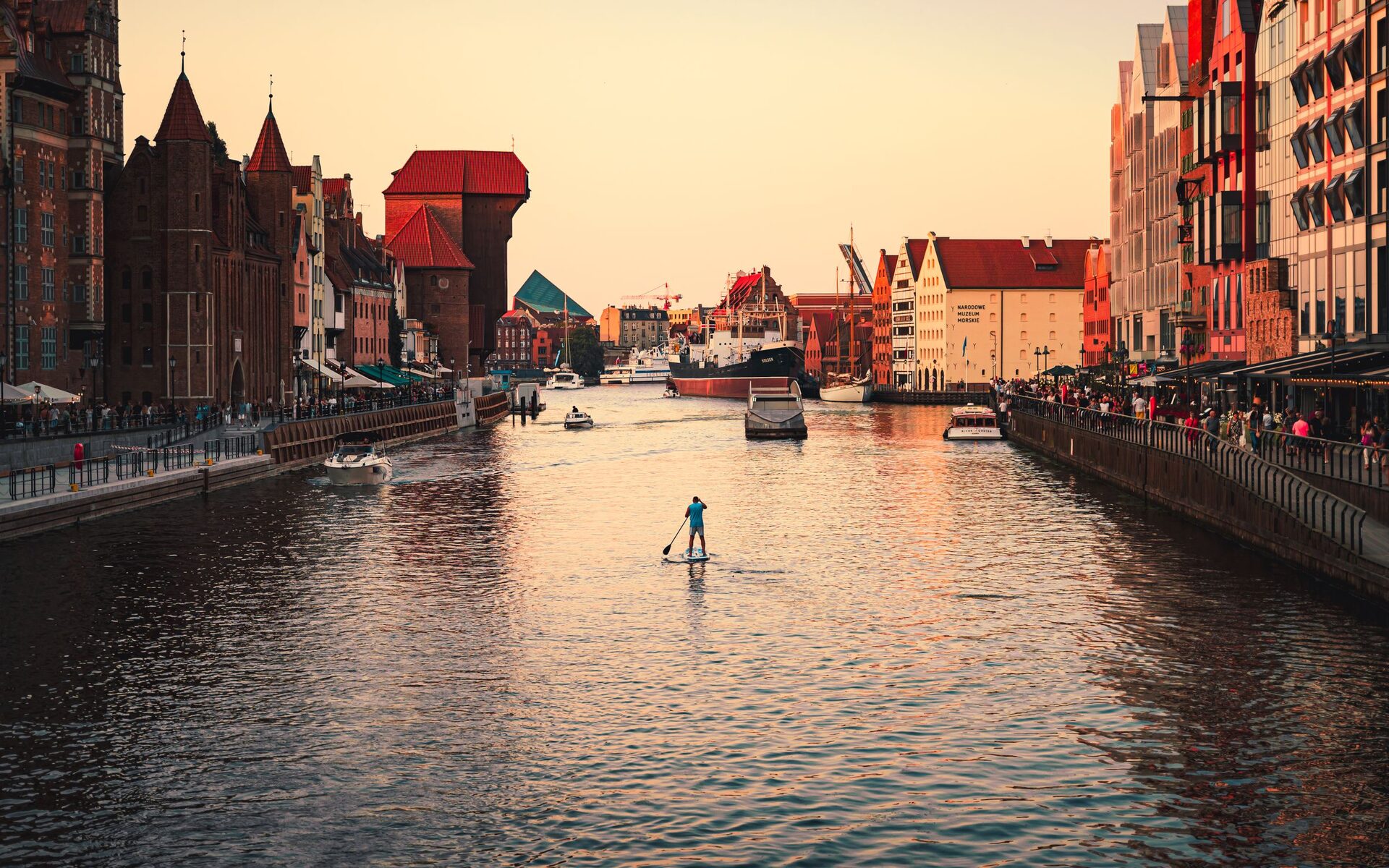 Sunset over the Motława river in Gdańsk, with the brick Crane and the gabled houses of the Long Riverfront and a paddleboarder on the water