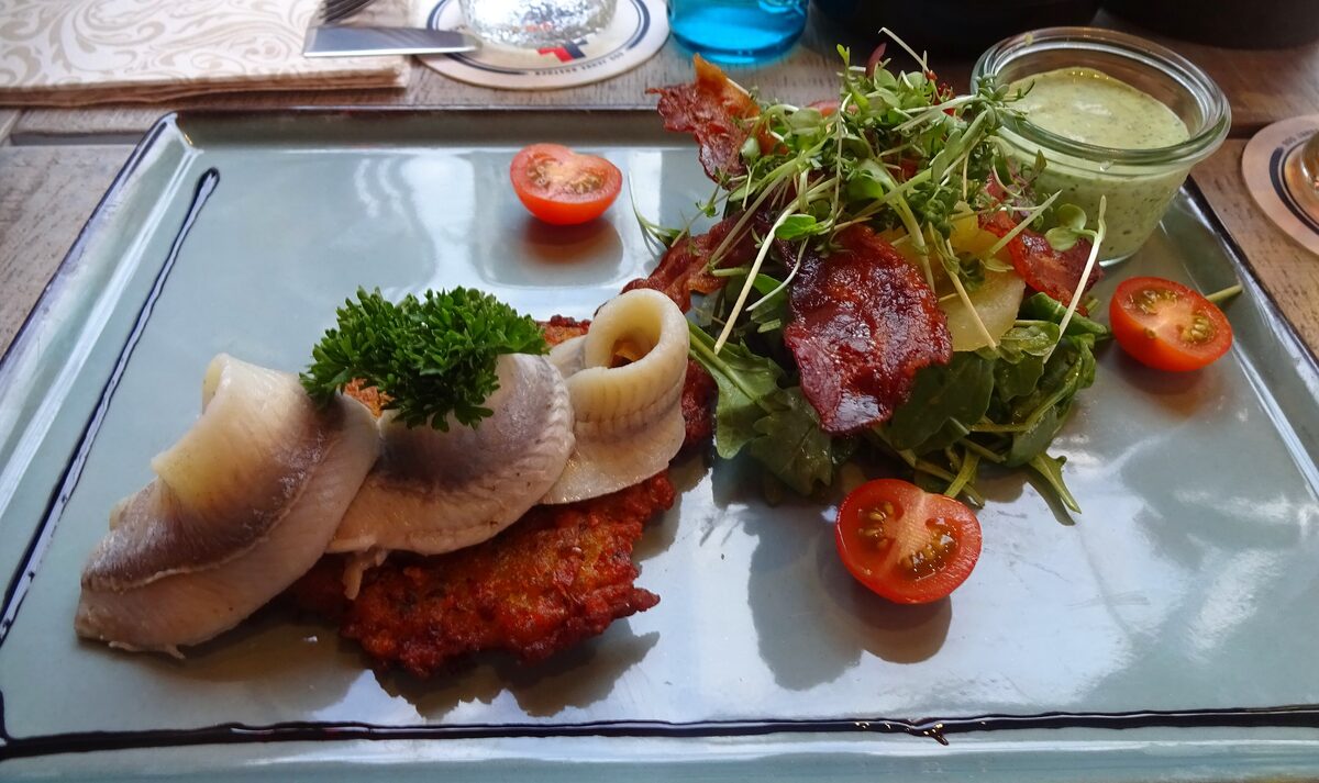 Pickled herring fillets on a potato pancake with salad and tomatoes