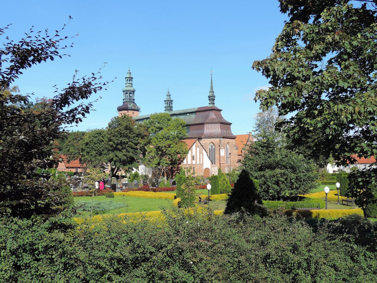 The Gothic church in Kartuzy with its curved roof, seen across a garden