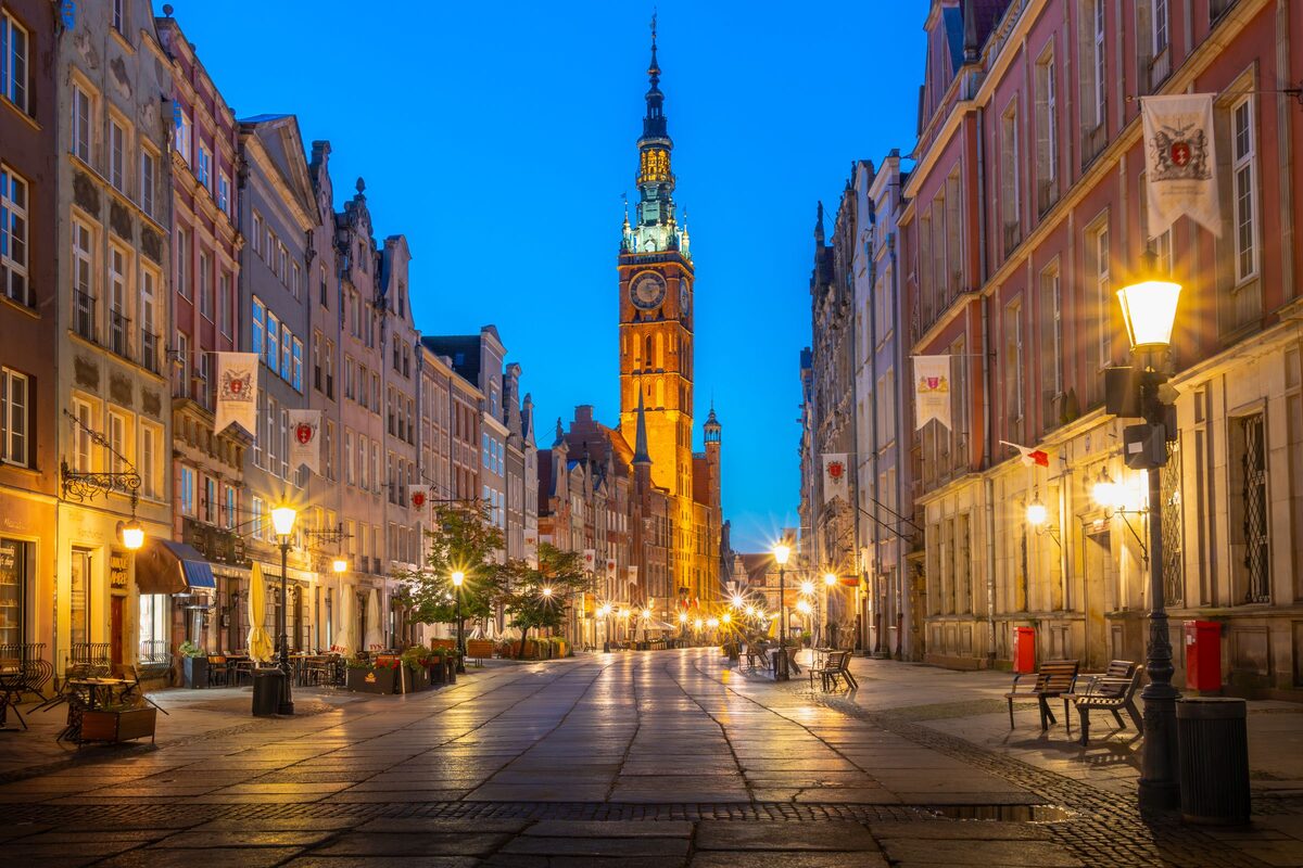 Długa street in Gdańsk at dusk, with lit lamps, gabled houses and the Main Town Hall tower at the end