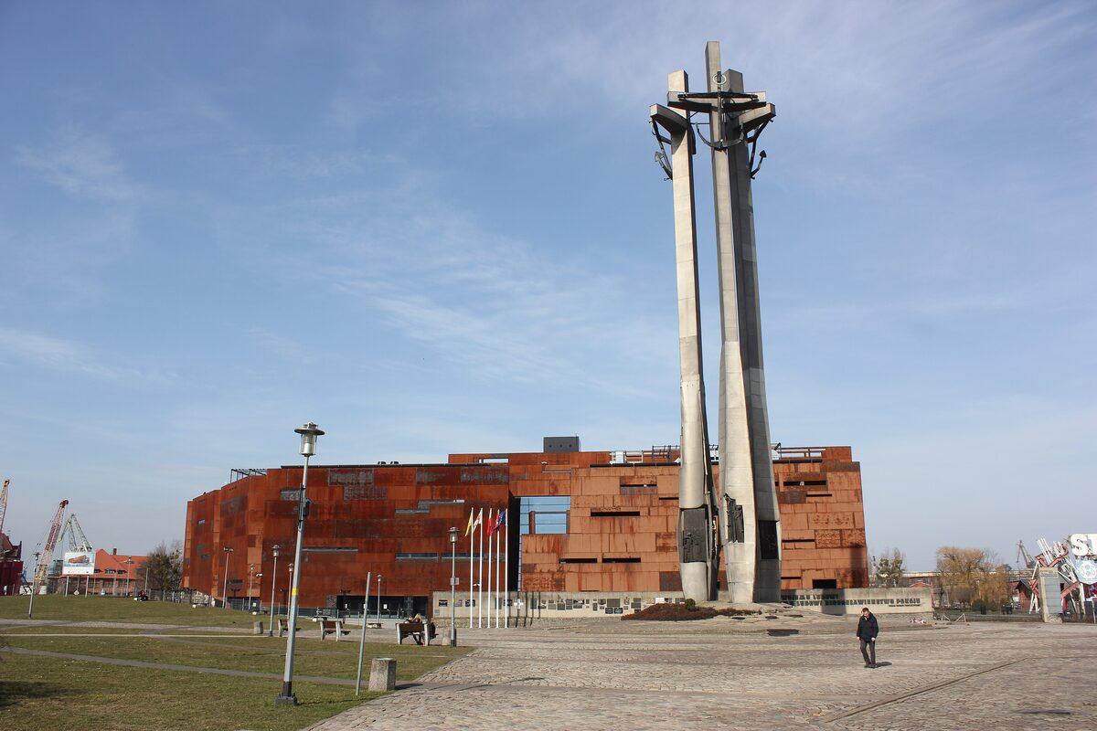 The three tall crosses of the Monument to the Fallen Shipyard Workers in front of the rust-colored European Solidarity Centre
