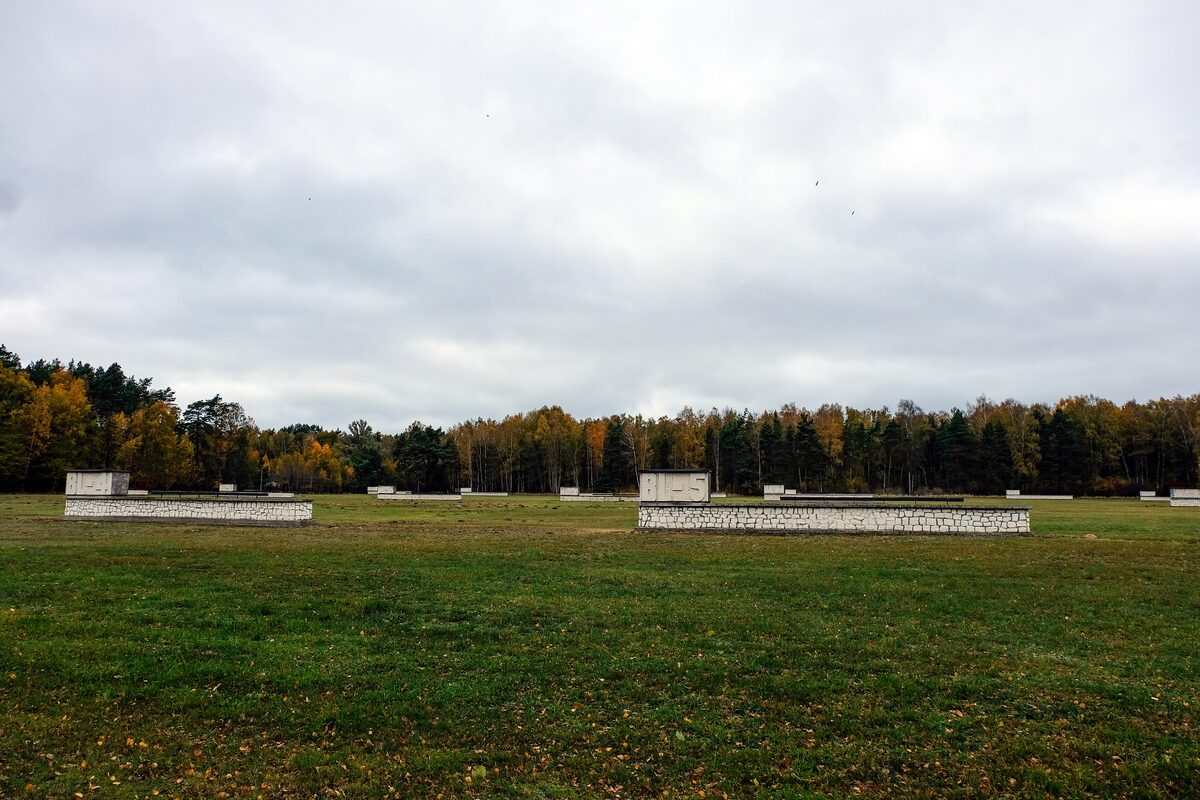 A wide field with the outlines of barracks at the Stutthof camp memorial, with forest behind