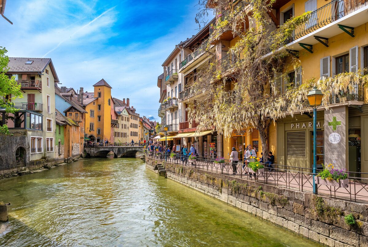 A canal in Annecy's old town with colorful houses lining the water and a stone bridge in the distance