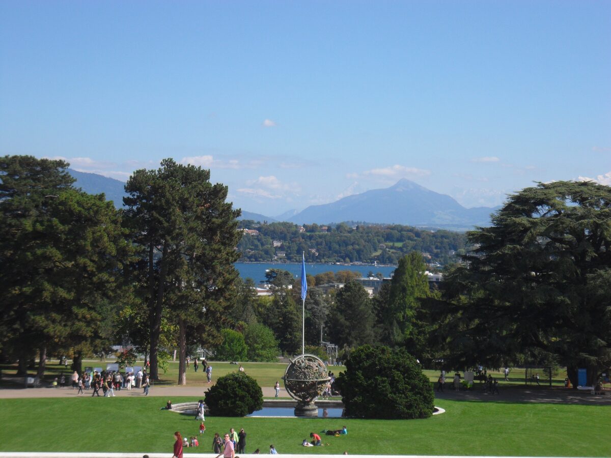 Ariana Park with its lawns, tall trees and a globe sculpture, with Lake Geneva visible beyond