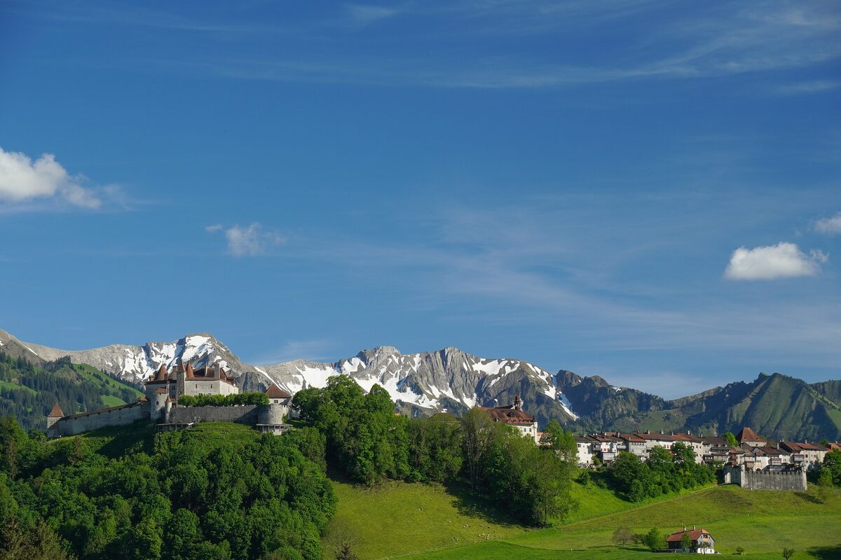 The hilltop town of Gruyères with its castle beneath snow-capped mountains and green meadows