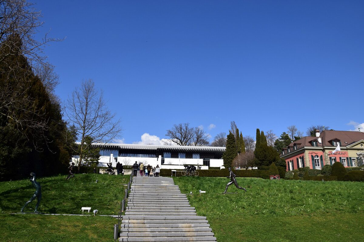 The white Olympic Museum building at the top of a long stone staircase across green lawns