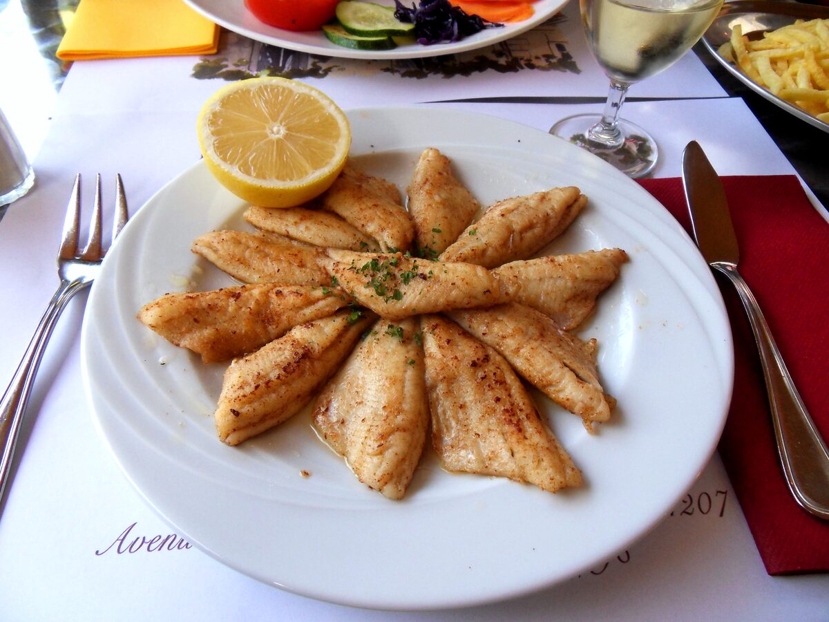 Fried perch fillets fanned out on a white plate with a lemon half