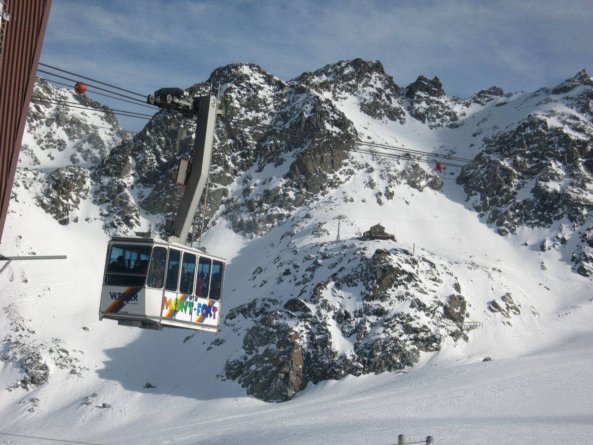 A gondola cabin climbing past snowy rock faces in the mountains above Verbier